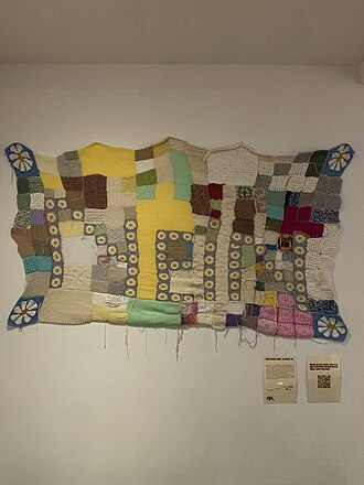 Eine bunte Decke, zusammengesetzt aus gestrickten und gehäkelten Quadraten, die die Aufschrift "Nein" zeigt.